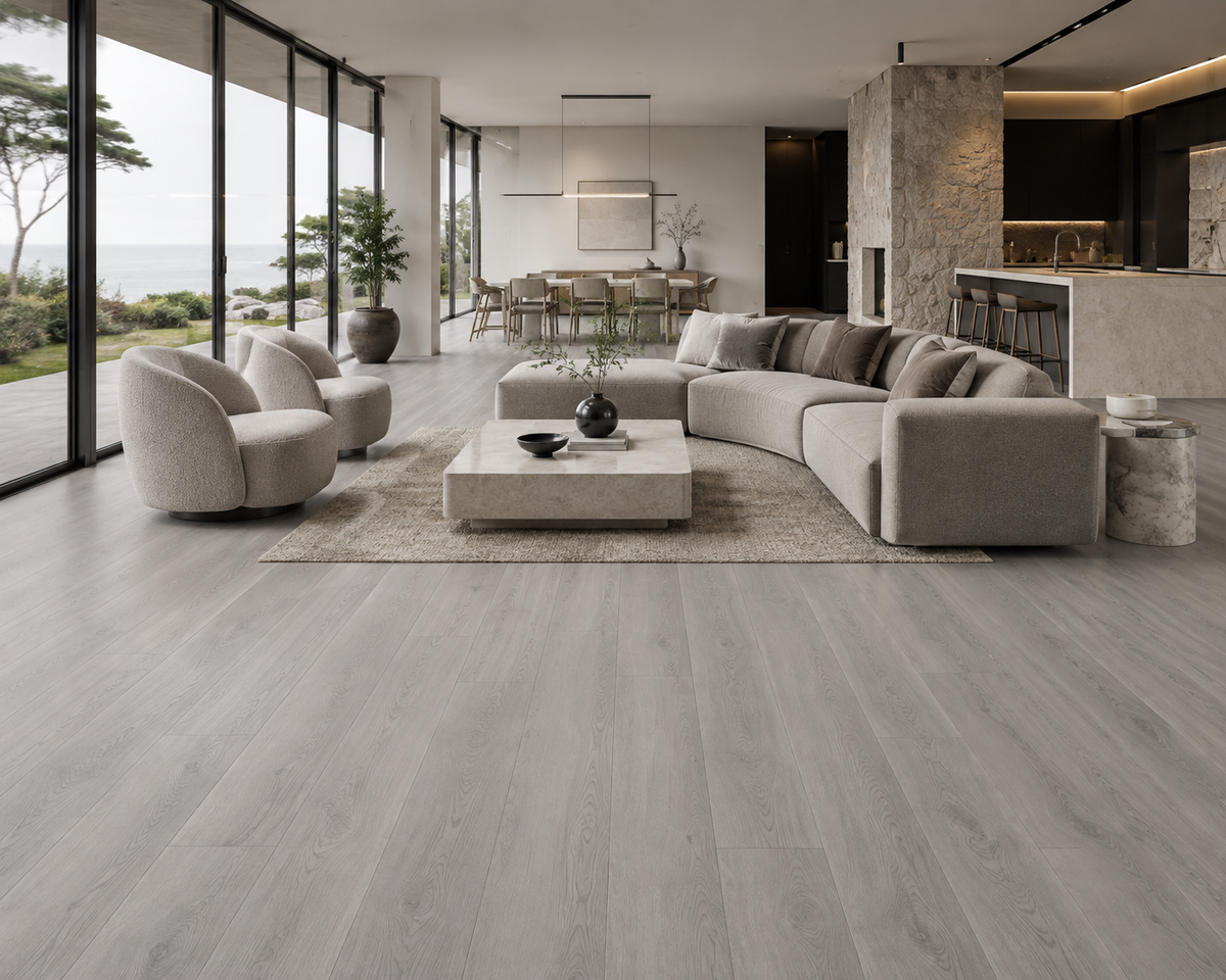 Light gray wood-look flooring shown in a modern, open-concept living room with a curved light gray sectional sofa, beige rug, and large floor-to-ceiling windows overlooking a garden.